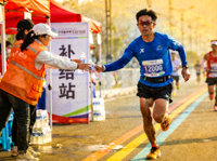 马拉松赛事补给站志愿者为跑者递水，长跑运动员奔跑姿态